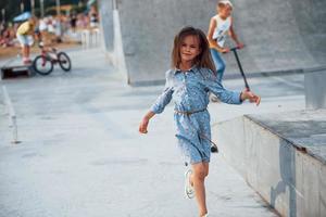 liten flicka i blå ha på sig Framställ för en kamera i de stad när lutande på de ramp foto