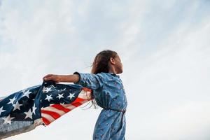 patriotisk kvinna unge med amerikan flagga i händer. mot molnig himmel foto