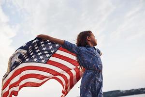 patriotisk kvinna unge med amerikan flagga i händer. mot molnig himmel foto