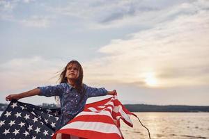 Fantastisk solnedgång. patriotisk kvinna unge med amerikan flagga i händer. mot molnig himmel foto