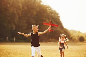 flicka och pojke har roligt utomhus med röd leksak flygplan i händer foto