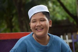 porträtt asiatisk muslim eller islamic pojke Sammanträde i de skola parkera och leende lyckligt, mjuk och selektiv fokus. foto