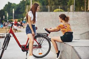 två ung kvinnor med cykel ha en Bra tid i de parkera nära de ramp foto
