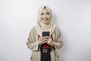 en porträtt av en Lycklig asiatisk kvinna bär en hijab och innehav henne telefon, isolerat förbi vit bakgrund foto