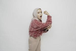 upphetsad asiatisk muslim kvinna bär en rosa Tröja och hijab som visar stark gest förbi lyft henne vapen och muskler leende stolt foto