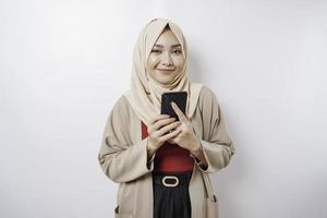 en porträtt av en Lycklig asiatisk kvinna bär en hijab och innehav henne telefon, isolerat förbi vit bakgrund foto