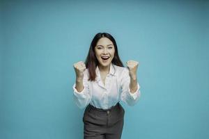 en ung asiatisk kvinna med en Lycklig framgångsrik uttryck bär vit skjorta isolerat förbi blå bakgrund foto
