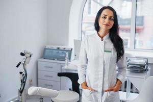 brunett kvinna läkare står i modern kontor och utseende på kamera foto