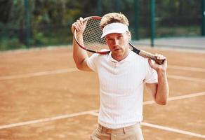 Framställ för en kamera. ung tennis spelare i sportigt kläder är på de domstol utomhus foto