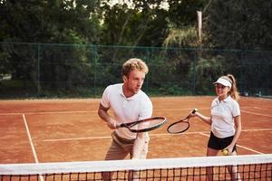 två människor i sport enhetlig spelar tennis tillsammans på de domstol foto