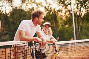 tar en ha sönder förbi lutande på de netto. två människor i sport enhetlig spelar tennis tillsammans på de domstol foto