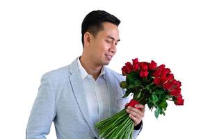 asiatisk man bär grå kostym innehav en bukett av röd ro isolerat i vit bakgrund för årsdag eller valentine dag begrepp. foto