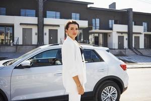 självsäker kvinna i vit formell ha på sig outdoots nära henne vit bil foto