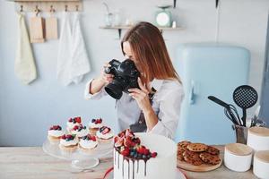 kvinna står i de kök och tar Foto av henne hemlagad småkakor och paj förbi använder sig av kamera
