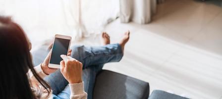 ung kvinna använder sig av smart telefon och avkopplande på soffa i levande rum på mysigt Hem i de morgon- foto