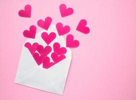 rosa hjärtan och vit kuvert på rosa bakgrund. romantisk meddelande, brev, gåva, hälsning kort för hjärtans dag begrepp. Semester festlig kreativ design kärlek sammansättning. flatlay, topp se foto