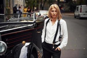 blond kvinna i svart retro kläder nära gammal årgång klassisk bil foto