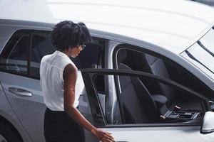 ung afrikansk amerikan kvinna i glasögon och med anteckningsblock står i de bil salong nära fordon foto