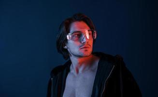 skön lång håriga varm man i glasögon är i de studio med blå neon belysning foto
