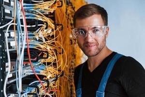 ung man i skyddande glasögon Arbetar med internet Utrustning och trådar i server rum foto