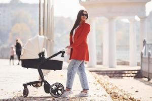 mor i röd täcka ha en promenad med henne unge i de pråm i de parkera på höst tid foto