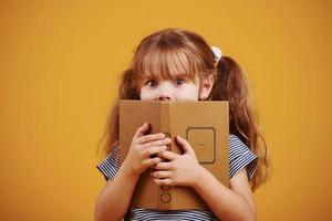 söt liten flicka med bok i händer i de studio mot gul bakgrund foto