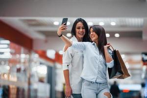 två ung kvinnor ha en handla dag tillsammans i de mataffär och framställning selfie foto