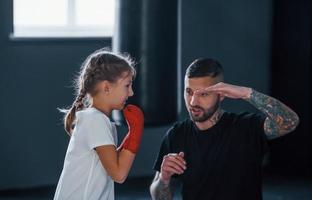 grundläggande slag. ung tatuerade boxning tränare lär söt liten flicka i de Gym foto