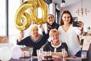 ballonger med siffra 60. senior kvinna med familj och vänner fira en födelsedag inomhus foto