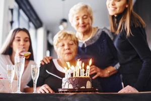 blåser de ljus. senior kvinna med familj och vänner fira en födelsedag inomhus foto