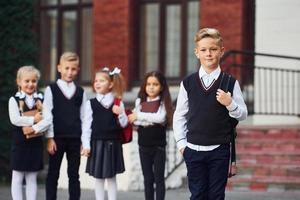 grupp av barn i skola enhetlig Framställ till de kamera utomhus tillsammans nära utbildning byggnad foto