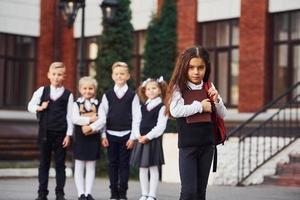 grupp av barn i skola enhetlig Framställ till de kamera utomhus tillsammans nära utbildning byggnad foto