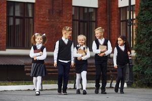 grupp av barn i skola enhetlig den där är utomhus tillsammans nära utbildning byggnad foto