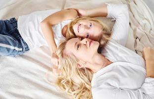 mor med henne dotter liggande ner tillsammans på de vit säng foto