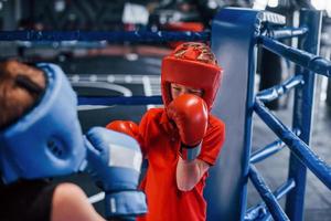 två Pojkar i skyddande Utrustning ha sparring och stridande på de boxning ringa foto