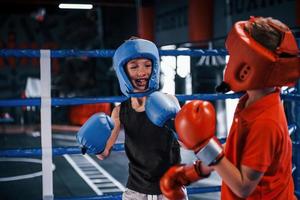 två Pojkar i skyddande Utrustning ha sparring och stridande på de boxning ringa foto