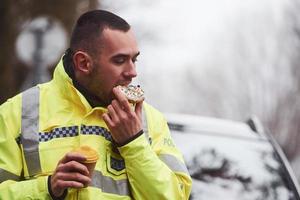 manlig polis officer i grön enhetlig tar en ha sönder med munk på de väg foto