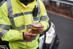 manlig polis officer i grön enhetlig tar en ha sönder med munk på de väg foto