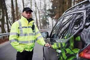 manlig polis officer i grön enhetlig stående nära fordon på de väg foto