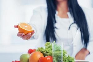 kvinna dietist i vit täcka innehav orange i hand foto