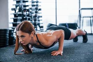 ung sportigt kvinna i svart kläder håller på med skjuta på Posten i de Gym foto