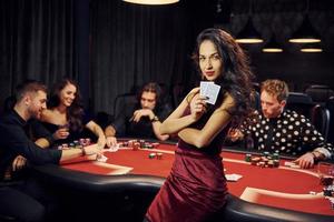 porträtt av skön kvinna. grupp av elegant ung människor den där spelar poker i kasino tillsammans foto