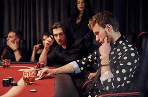 sida se av grupp av elegant ung människor den där spelar poker i kasino tillsammans foto