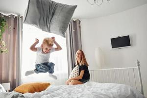 mor spelar kudde bekämpa med henne son i sovrum på dagtid foto