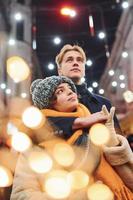 positiv ung par i värma kläder fattande varje Övrig på jul dekorerad gata foto
