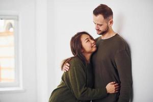 Lycklig mång etnisk par i tillfällig kläder fattande varje Övrig inomhus i de studio. caucasian kille med asiatisk flickvän foto