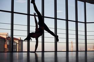 silhuett av ung sportig kvinna i sportkläder den där håller på med akrobatisk knep i de Gym foto
