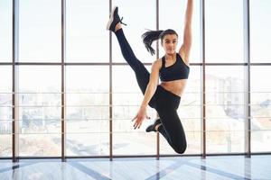 ung sportig kvinna i sportkläder Hoppar och håller på med atletisk knep mot fönster i de luft foto