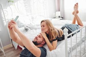ung gift par framställning en selfie förbi använder sig av telefon i sovrum på dagtid foto
