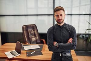 modern affärsman stående inomhus i kontor med hans vapen korsade foto